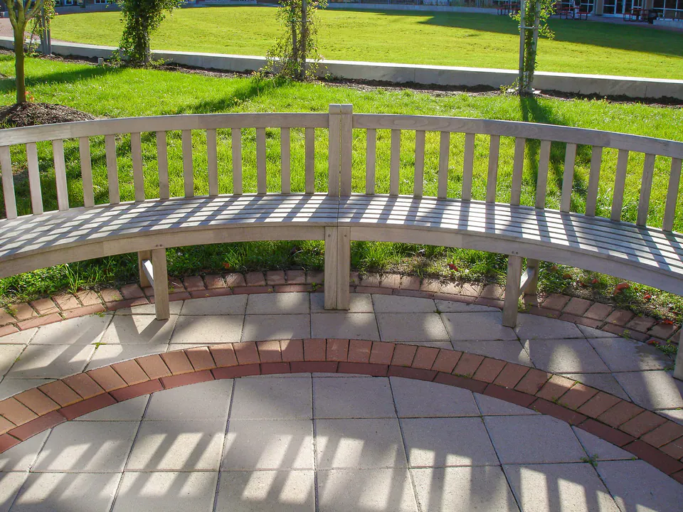 Curved campus bench with paver circle, brick banding, lawn edge, and shadow pattern